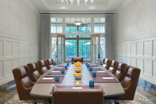 An elegant boardroom with a large wooden oval table surrounded by brown leather chairs, arranged for a meeting.