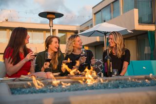 Group of women around the fire outside during golden hour enjoying wine.