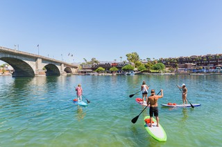 Few people paddleboarding on Lake Havasu with the London Bridge in the background.