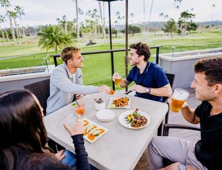 Group of people eating and drinking outdoors with golf course view.