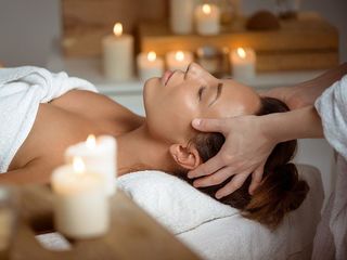 Woman receiving a head massage while lying on a massage table, surrounded by lit candles in a spa setting.
