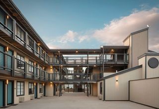 Exterior view of a modern hotel featuring light-colored wooden siding, dark metal railings, and connecting walkways.
