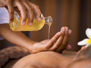 Hands pouring golden massage oil from a glass bottle onto open hands during a spa treatment.