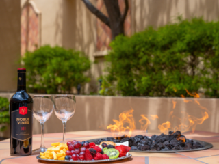 Firepit in outdoor courtyard with a bottle of wine, wine glasses, and a fruit platter.