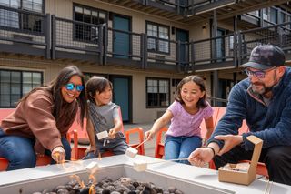 A family happily roasts marshmallows over a fire pit on a patio.