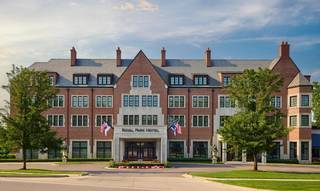 Exterior view of the Royal Park Hotel, a multi-story brick building with a slate roof, centered on a circular driveway, flanked by green trees and well-maintained landscaping.