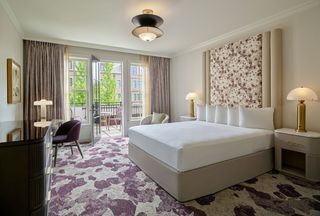 Executive Terrace Room featuring a large bed with a floral patterned headboard, bedside tables with lamps, and a view of a balcony with outdoor seating, with purple patterned carpet.