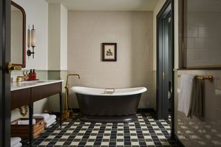 Elegant bathroom interior featuring a black and white bathtub, dark wood vanity with marble countertop, vintage brass fixtures, framed artwork, and a black, white, and green checkered floor.