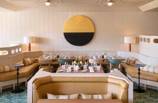 Dining room with booths, tables set for meals, and a large circular wall art piece.