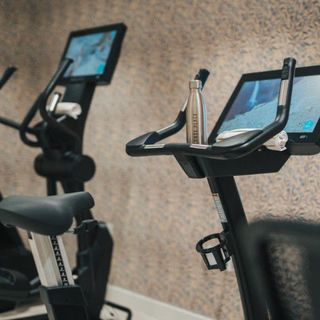 Close-up of two stationary exercise bikes with large screens, one with a metal water bottle resting on the handlebars.
