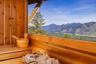 Interior of a wooden sauna with a window overlooking a vast mountain landscape under a blue sky.